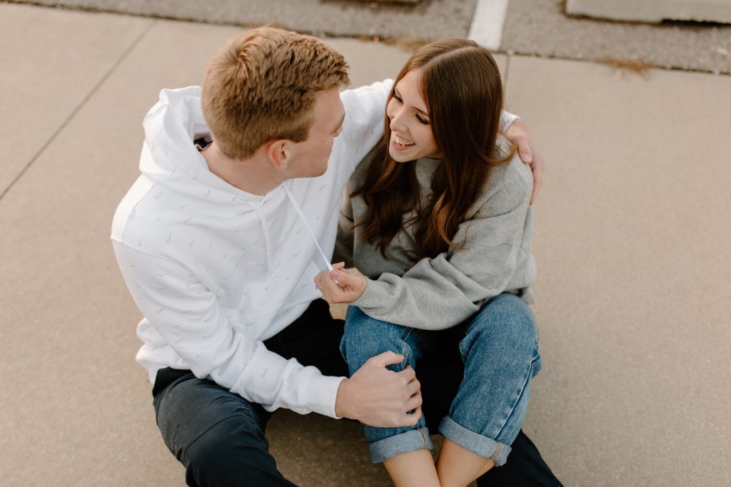 Couple sitting on cement, engaged couple cuddling, casual engagement photos